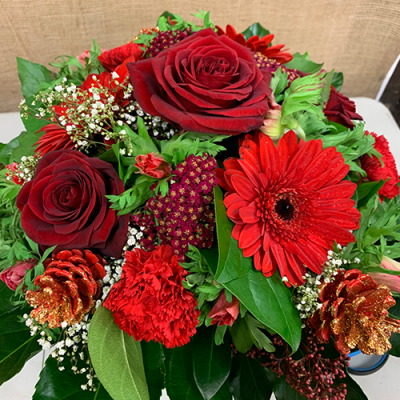 Merry Medley - A lovely Christmas arrangement in created using the fresh blooms of the day in reds and green with complementary foliage.